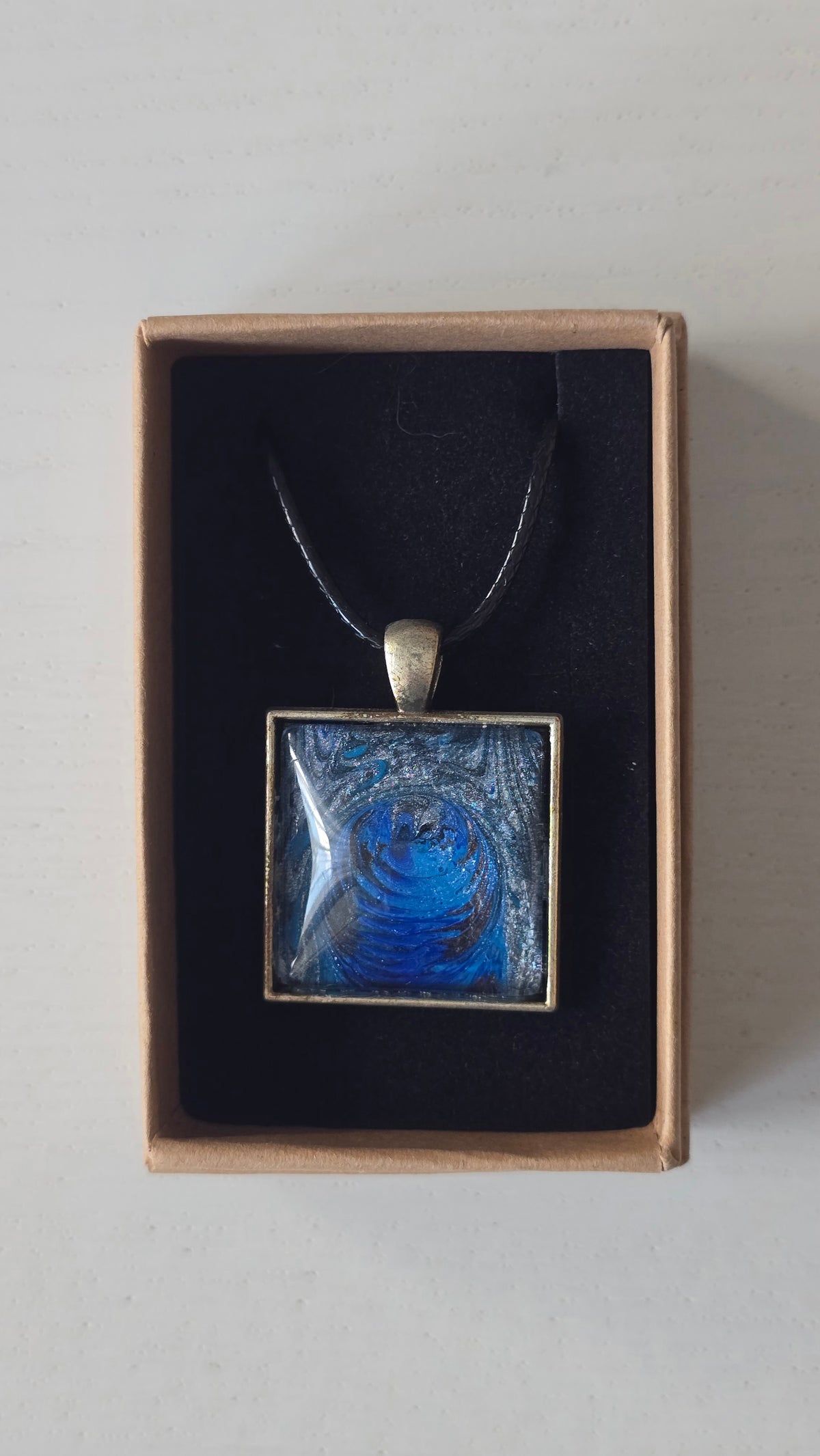 Quadratische Cabochon-Kette mit spiralförmigem, abstraktem Muster in intensivem Blau, Türkis und schimmerndem Silber.