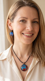 Frau trägt rundes Cabochon-Schmuckset mit Anhänger und Ohrringen an schwarzem Band, mit verzweigtem Muster in leuchtendem Cyan, Blau, Dunkelrot und Burgunder.
