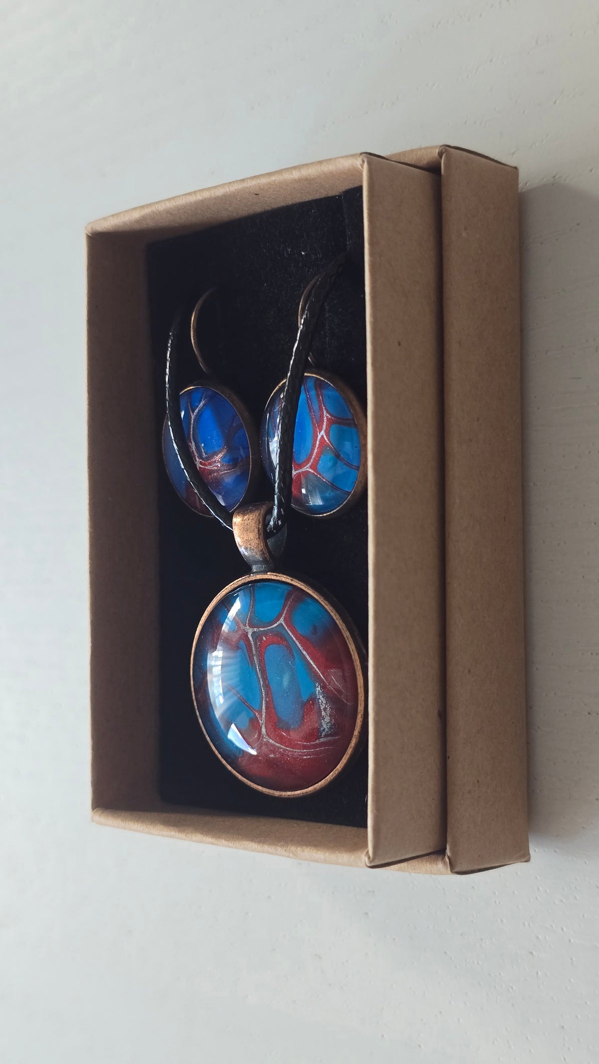 Rundes Cabochon-Schmuckset mit Anhänger und Ohrringen an schwarzem Band, mit verzweigtem Muster in leuchtendem Cyan, Blau, Dunkelrot und Burgunder.