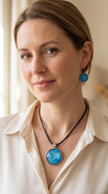 Frau trägt rundes Cabochon-Schmuckset mit Anhänger und Ohrringen an schwarzem Band, mit organischem Muster in Türkis, Cyan und Blau sowie silbernem Schimmer.