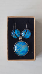 Rundes Cabochon-Schmuckset mit Anhänger und Ohrringen an schwarzem Band, mit organischem Muster in Türkis, Cyan und Blau sowie silbernem Schimmer.