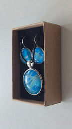 Rundes Cabochon-Schmuckset mit Anhänger und Ohrringen an schwarzem Band, mit organischem Muster in Türkis, Cyan und Blau sowie silbernem Schimmer.