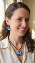 Frau trögt cabochon Schmuckset Solas Crystal Wave mit runder Kette und passenden Ohrringen in leuchtendem Blau, Türkis und Weiss mit silberfarbenen Fassungen.