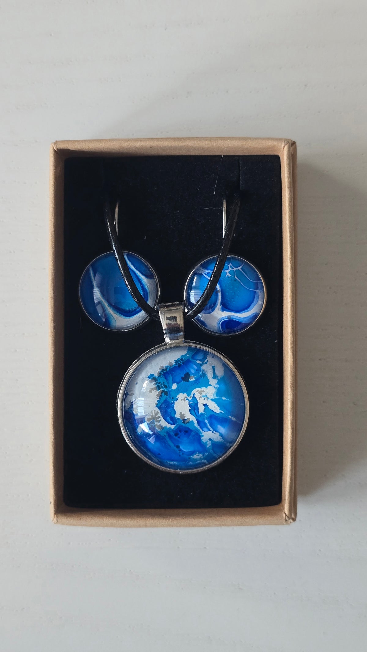 Cabochon Schmuckset Solas Crystal Wave mit runder Kette und passenden Ohrringen in leuchtendem Blau, Türkis und Weiss mit silberfarbenen Fassungen.