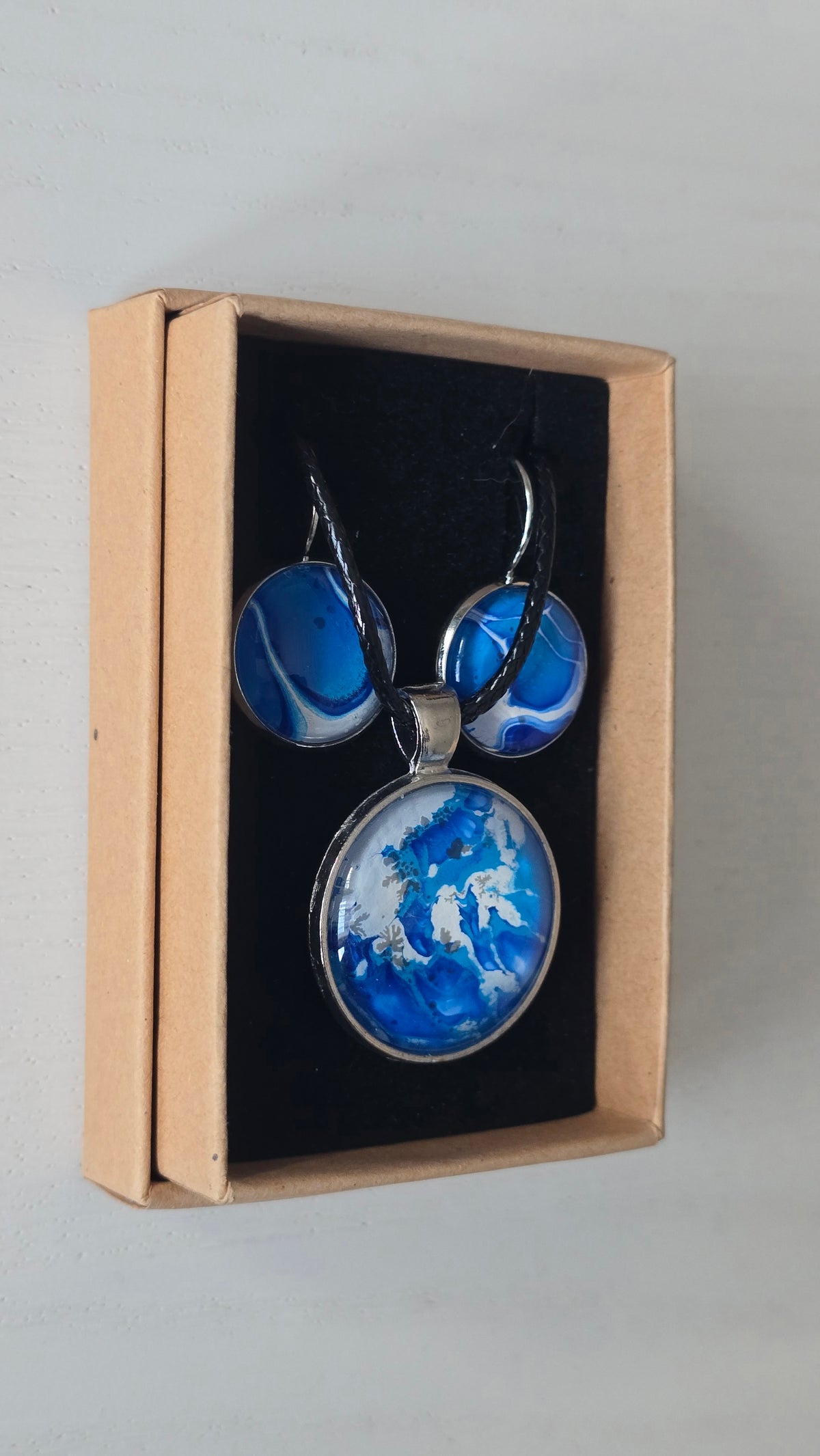 Cabochon Schmuckset Solas Crystal Wave mit runder Kette und passenden Ohrringen in leuchtendem Blau, Türkis und Weiss mit silberfarbenen Fassungen.