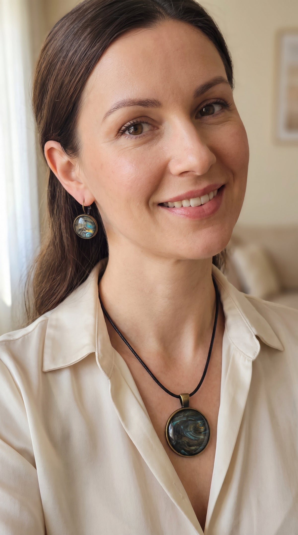 Frau trägt rundes Cabochon Schmuckset mit Kette und zwei Ohrringen, abstraktes Muster in Schwarz, Türkis, Blaugrün und Gold mit fliessenden Strukturen.