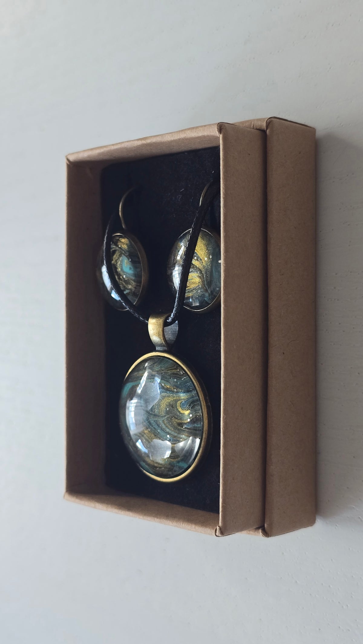 Rundes Cabochon Schmuckset mit Kette und zwei Ohrringen, abstraktes Muster in Schwarz, Türkis, Blaugrün und Gold mit fliessenden Strukturen.