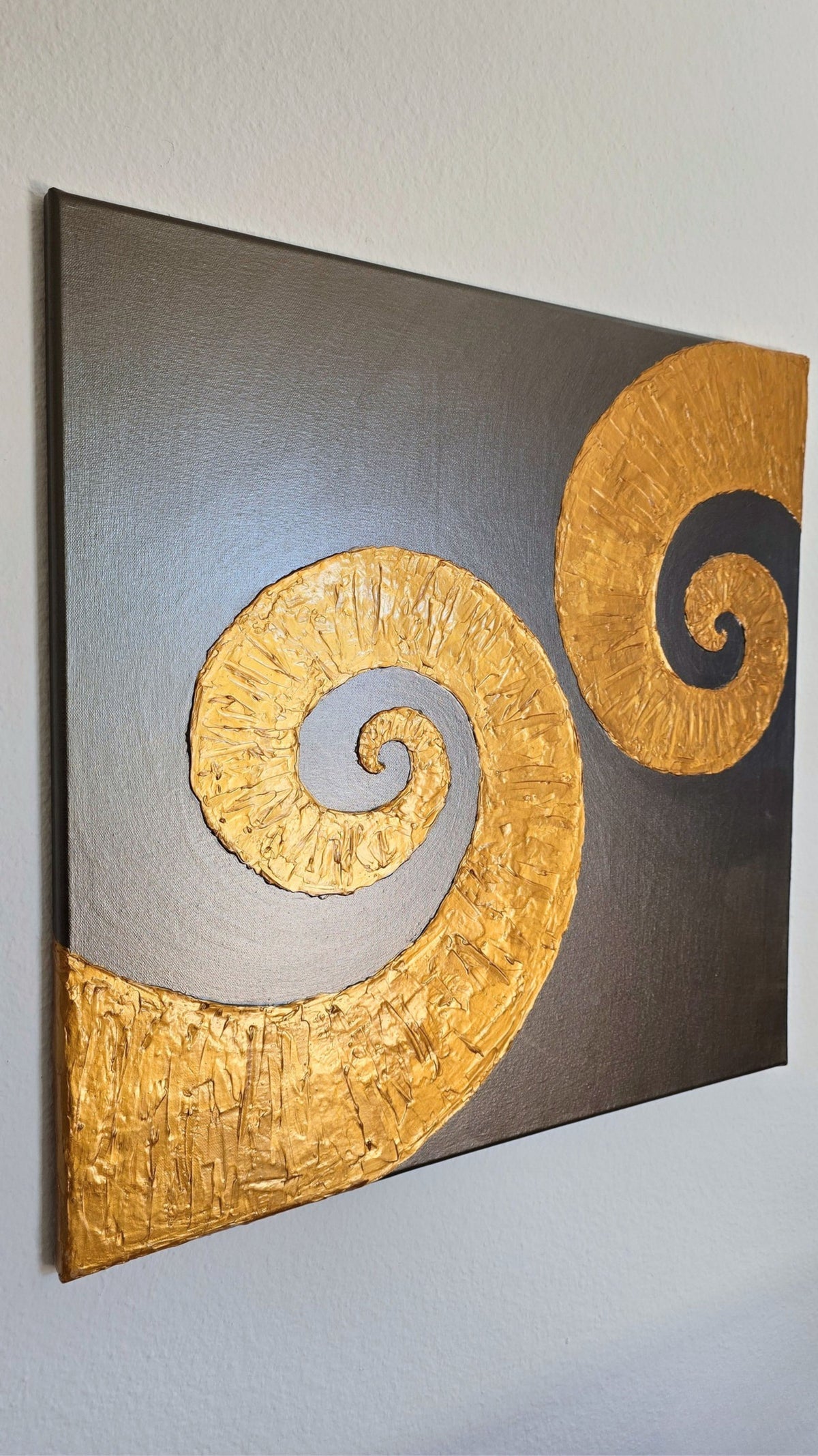 Quadratisches Leinwandbild mit warmgrauem Hintergrund und zwei grossen, plastisch strukturierten goldenen Spiralen.