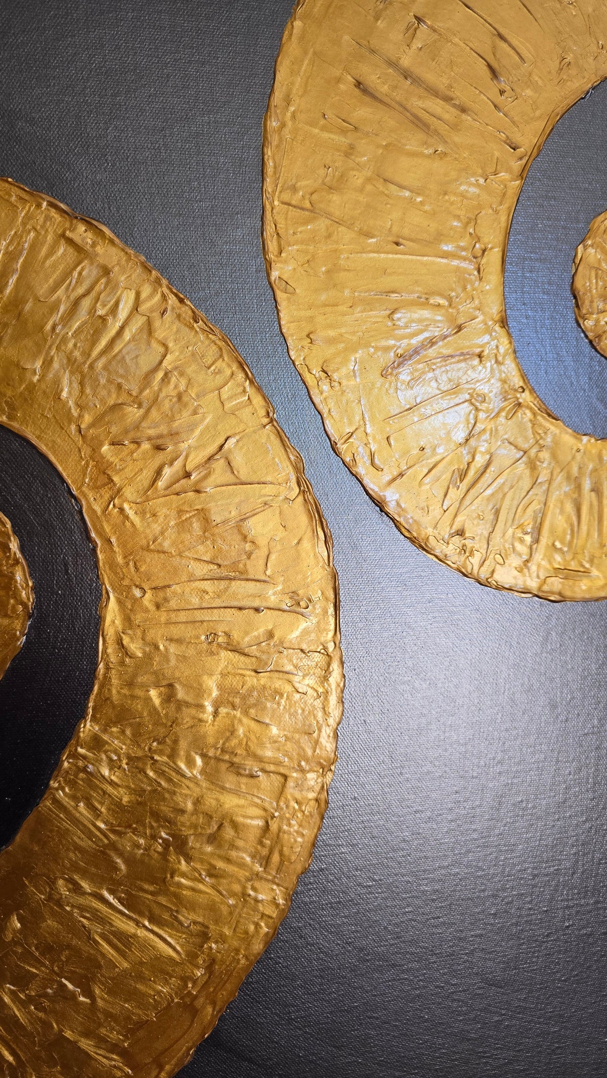 Quadratisches Leinwandbild mit warmgrauem Hintergrund und zwei grossen, plastisch strukturierten goldenen Spiralen.