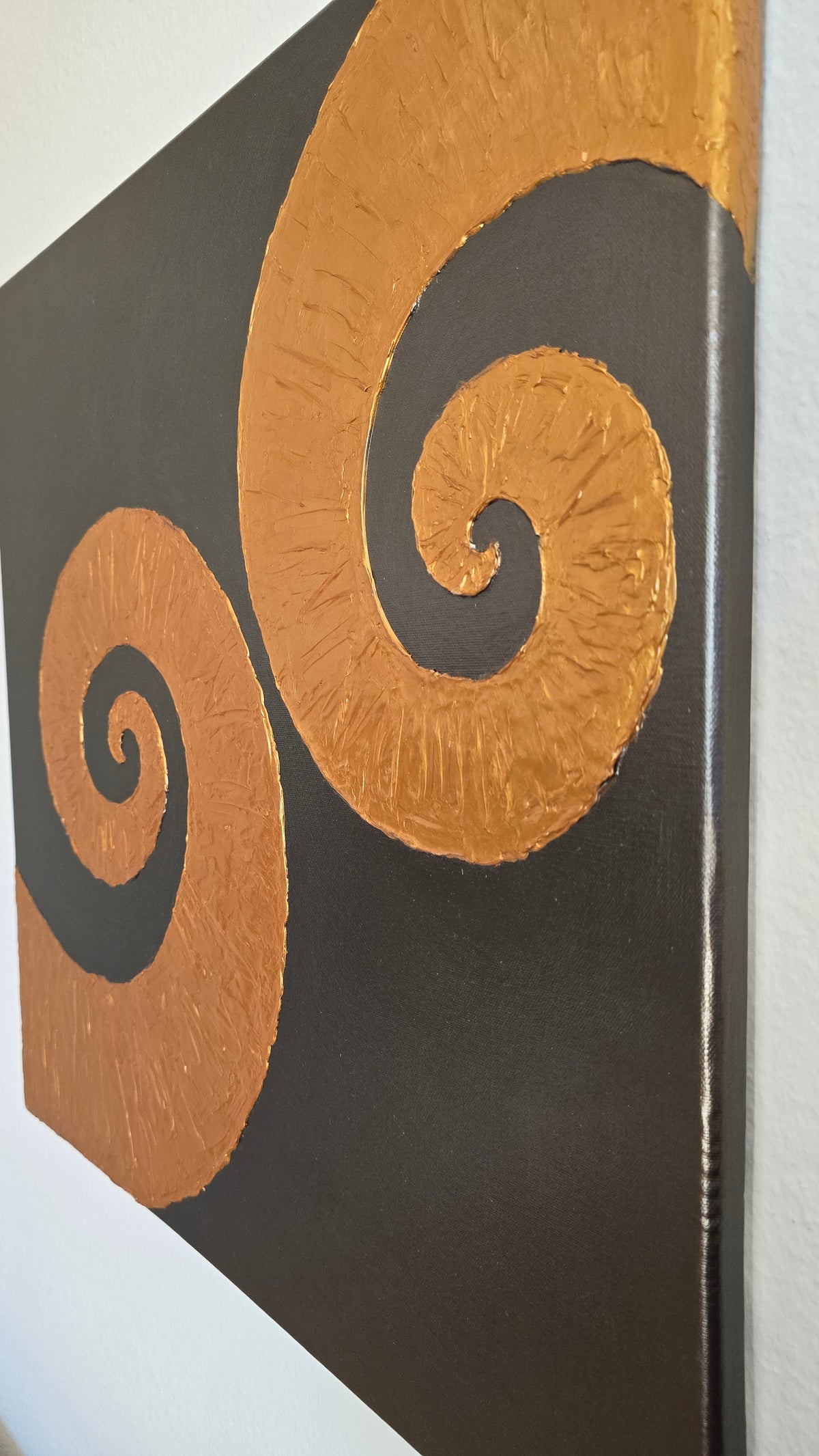 Quadratisches Leinwandbild mit warmgrauem Hintergrund und zwei grossen, plastisch strukturierten goldenen Spiralen.