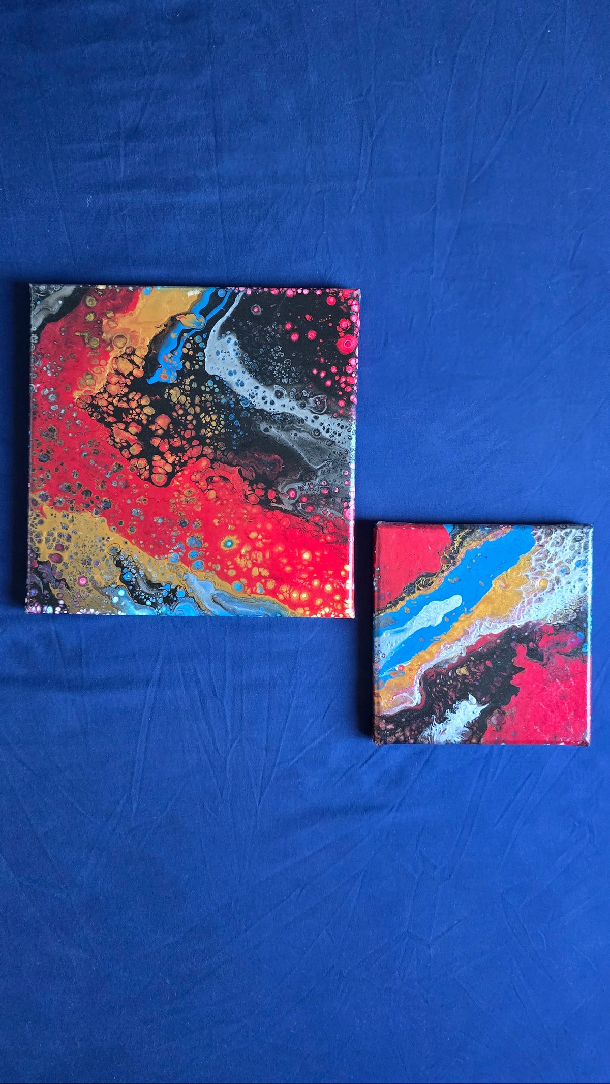 Drei abstrakte Leinwandbilder in unterschiedlichen Grössen mit fliessenden Farbflächen und feinen Zellstrukturen in Rot, Blau, Gold, Schwarz und Weiss.