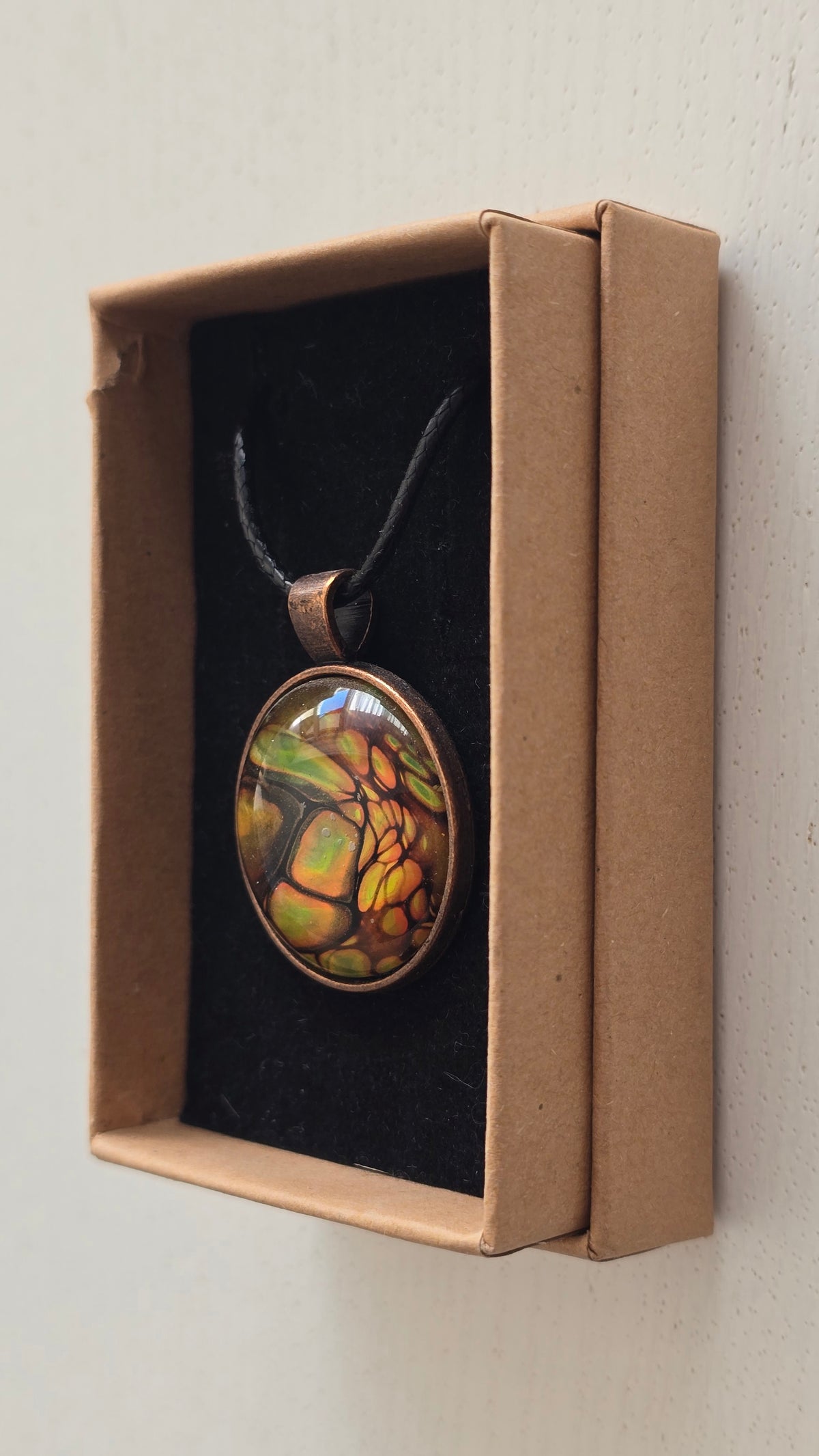Runde Cabochon Kette Solas Forest Flame in Grün, Orange und Gold mit dunklen Strukturen, bronzefarbener Fassung und schwarzem Band.