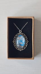 Ovale Cabochon Kette Solas Frozen Current in leuchtendem Blau, Silber und Grau mit verzierter silberfarbener Fassung und Metallkette.