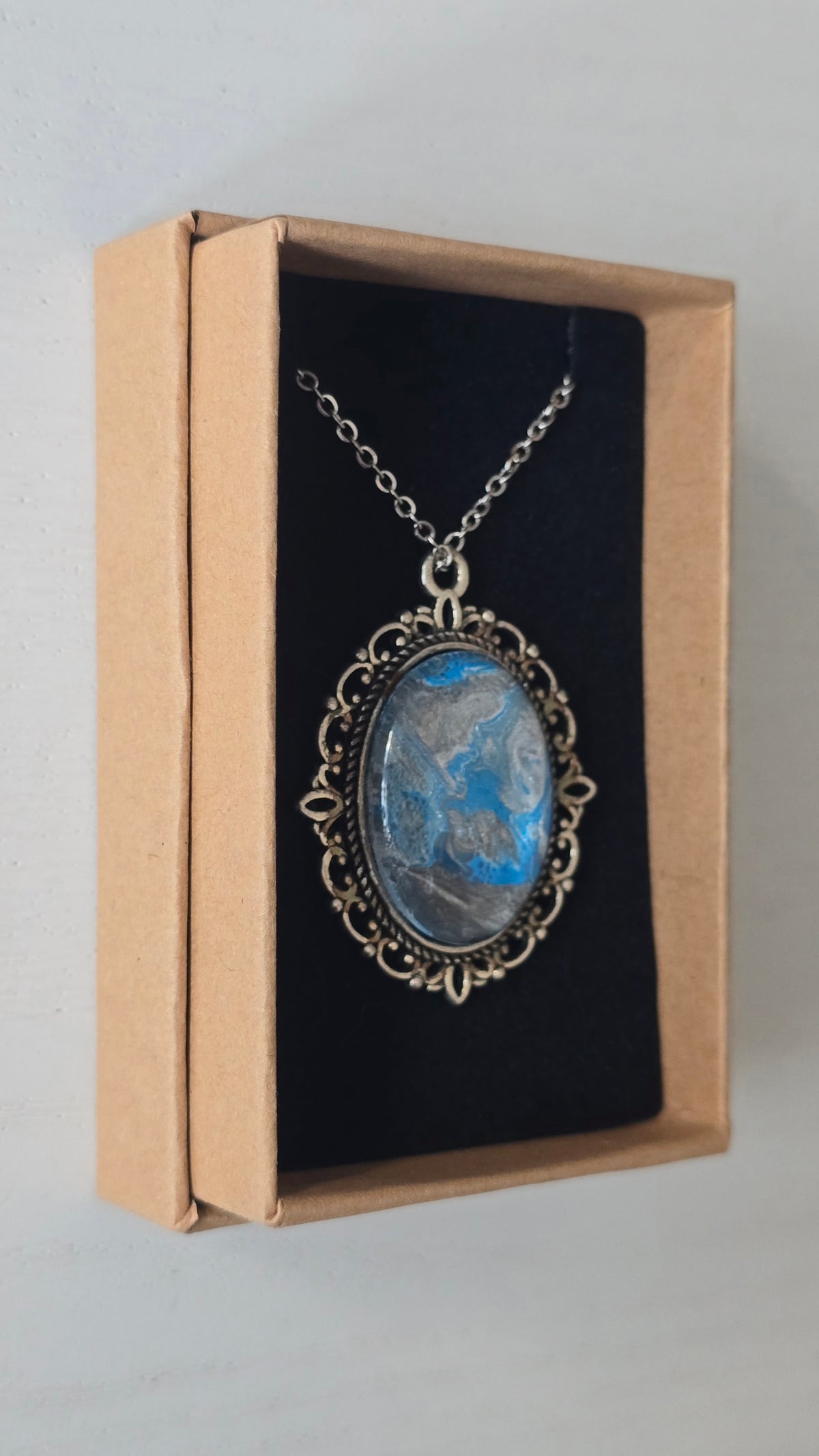 Ovale Cabochon Kette Solas Frozen Current in leuchtendem Blau, Silber und Grau mit verzierter silberfarbener Fassung und Metallkette.