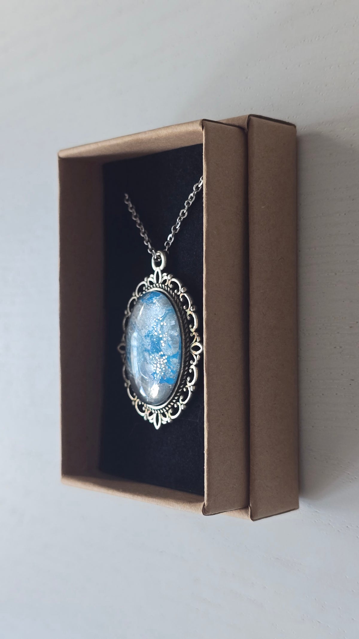 Ovale Cabochon Kette Solas Frozen Current in leuchtendem Blau, Silber und Grau mit verzierter silberfarbener Fassung und Metallkette.