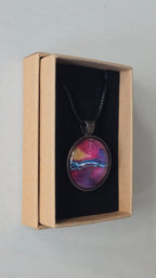 Runder Cabochon-Anhänger an schwarzem Band mit geschichtetem Muster in Fuchsia, Pink, Violett, Blau, Türkis und einem goldenen Akzent.