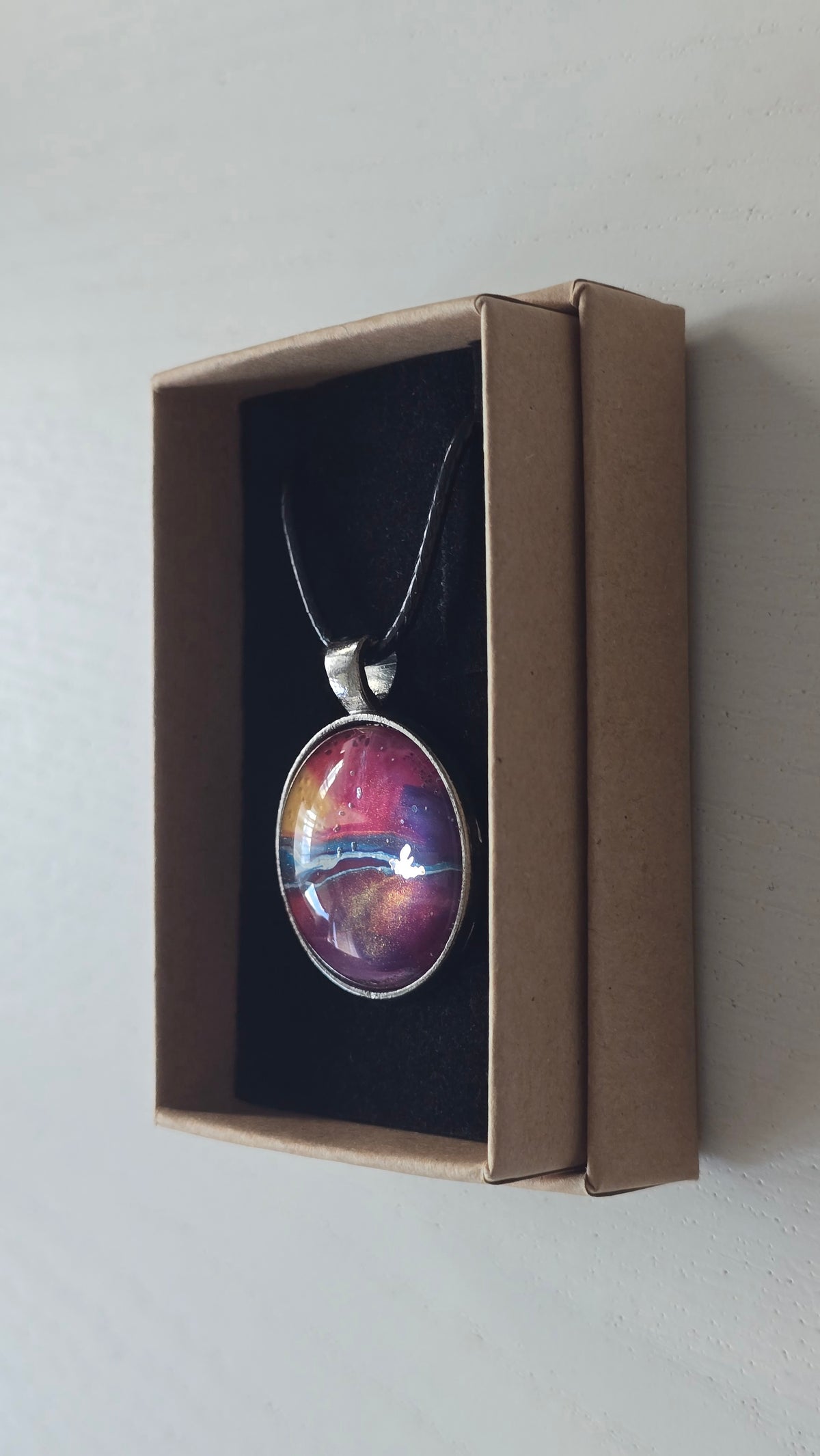 Runder Cabochon-Anhänger an schwarzem Band mit geschichtetem Muster in Fuchsia, Pink, Violett, Blau, Türkis und einem goldenen Akzent.