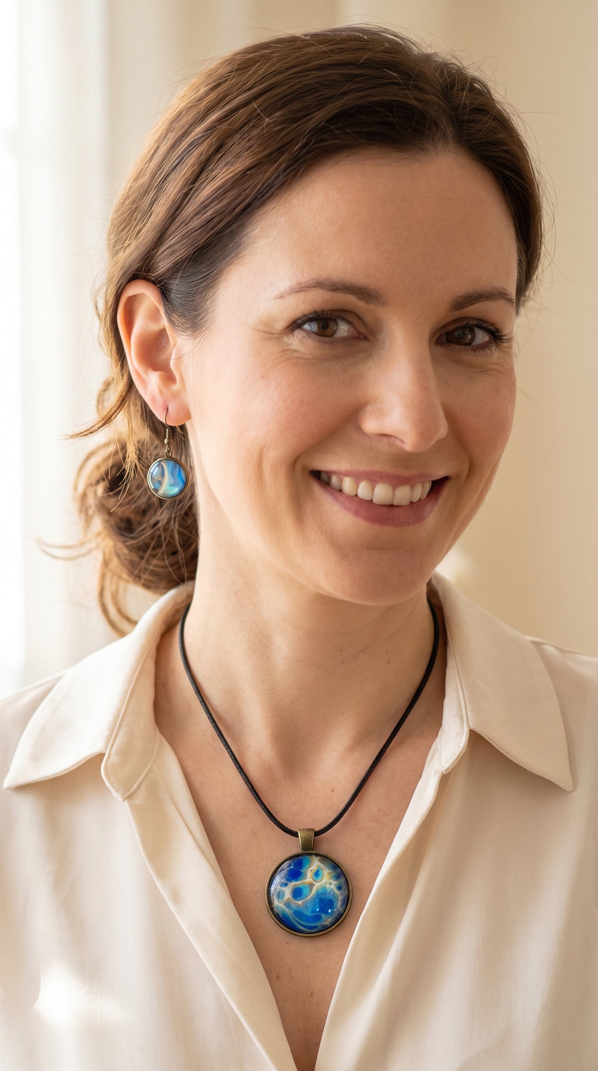 Frau trägt rundes Cabochon-Schmuckset mit Anhänger und Ohrringen an schwarzem Band, mit organischem Muster in Blau, Türkis und Aquatönen sowie goldenen Akzenten.