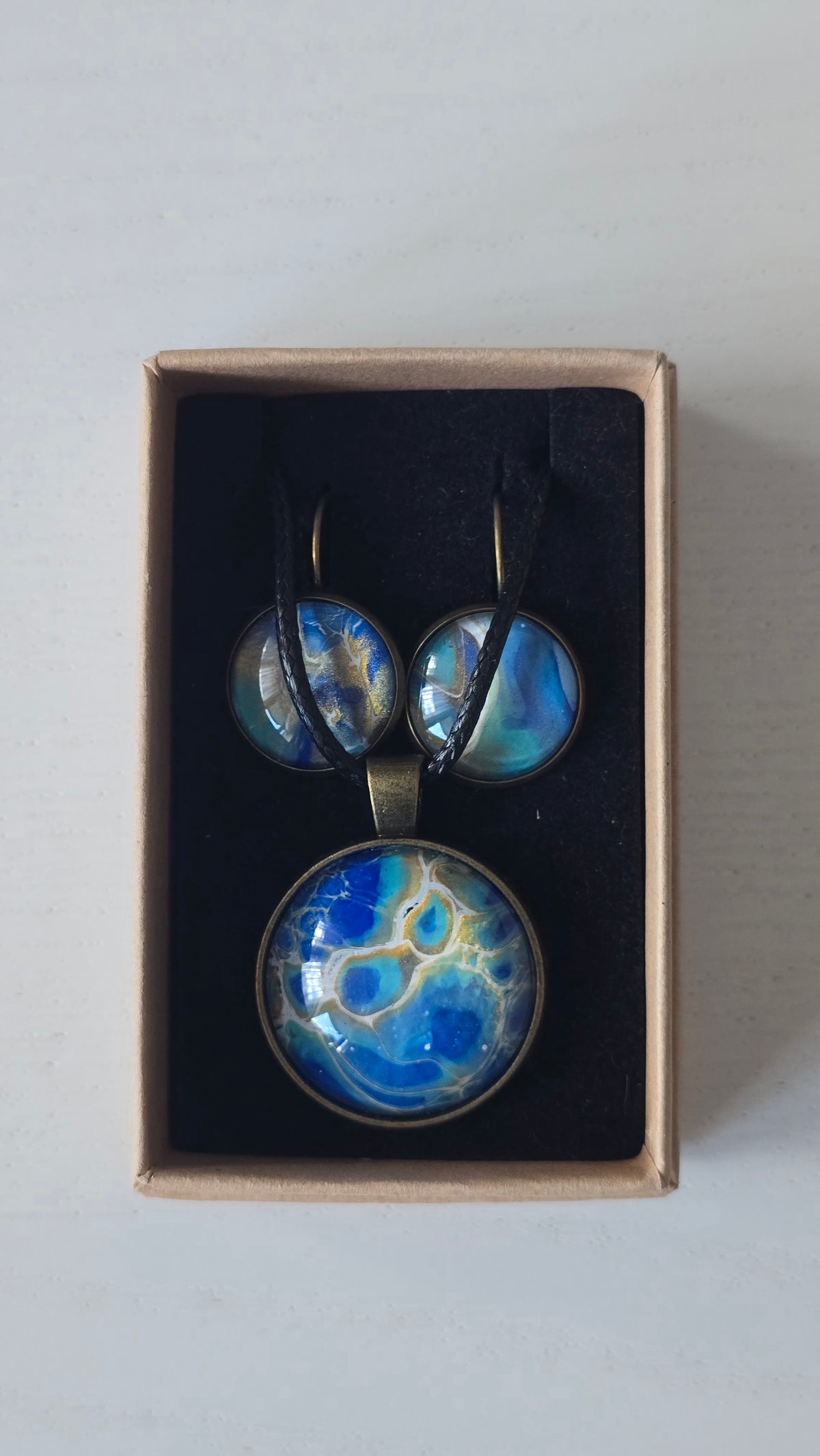 Rundes Cabochon-Schmuckset mit Anhänger und Ohrringen an schwarzem Band, mit organischem Muster in Blau, Türkis und Aquatönen sowie goldenen Akzenten.