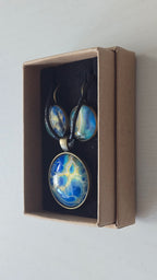 Rundes Cabochon-Schmuckset mit Anhänger und Ohrringen an schwarzem Band, mit organischem Muster in Blau, Türkis und Aquatönen sowie goldenen Akzenten.