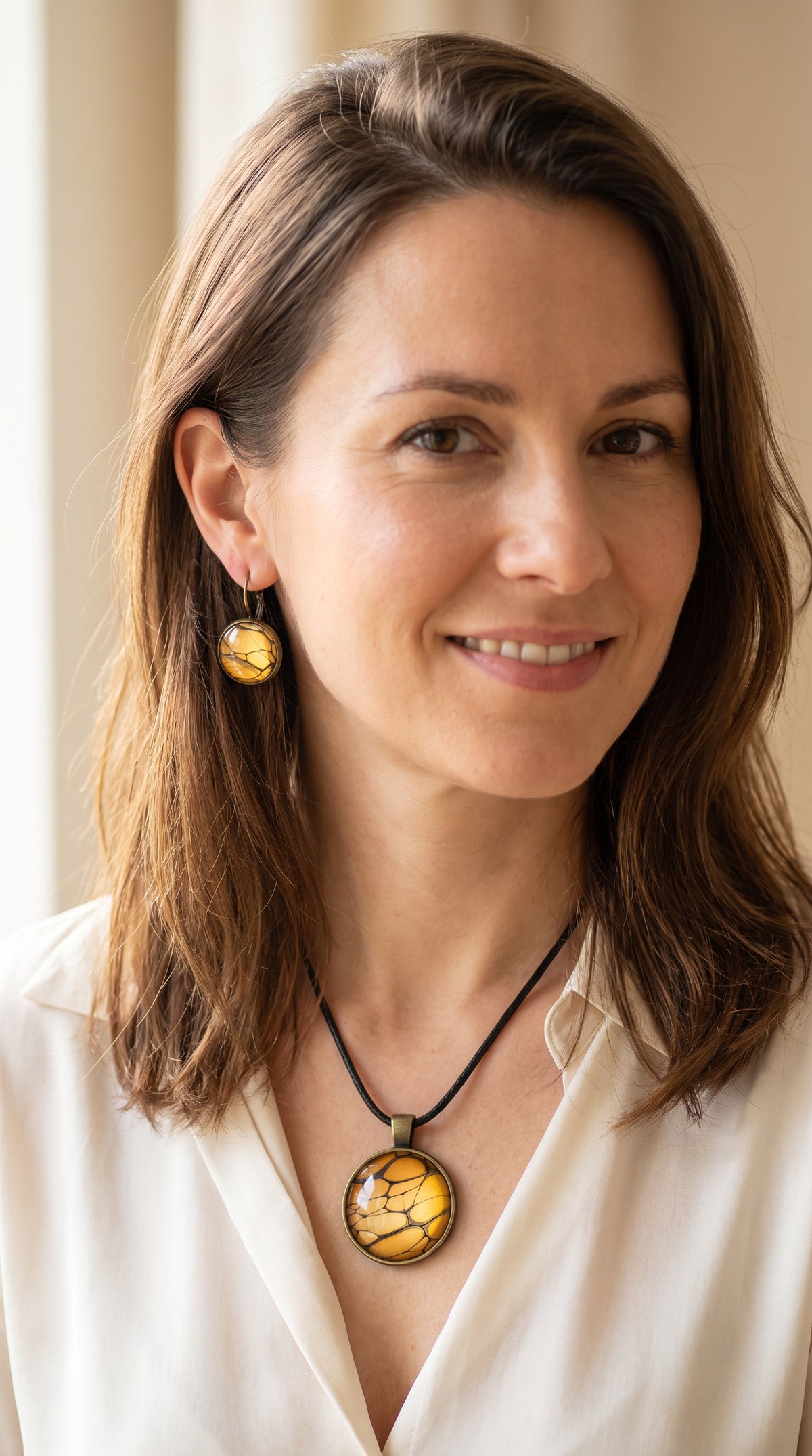 Frau trägt rundes Cabochon-Schmuckset mit Halskettenanhänger und passenden Ohrringen in warmen Gold- und Bernsteintönen mit feinen dunklen Linien.