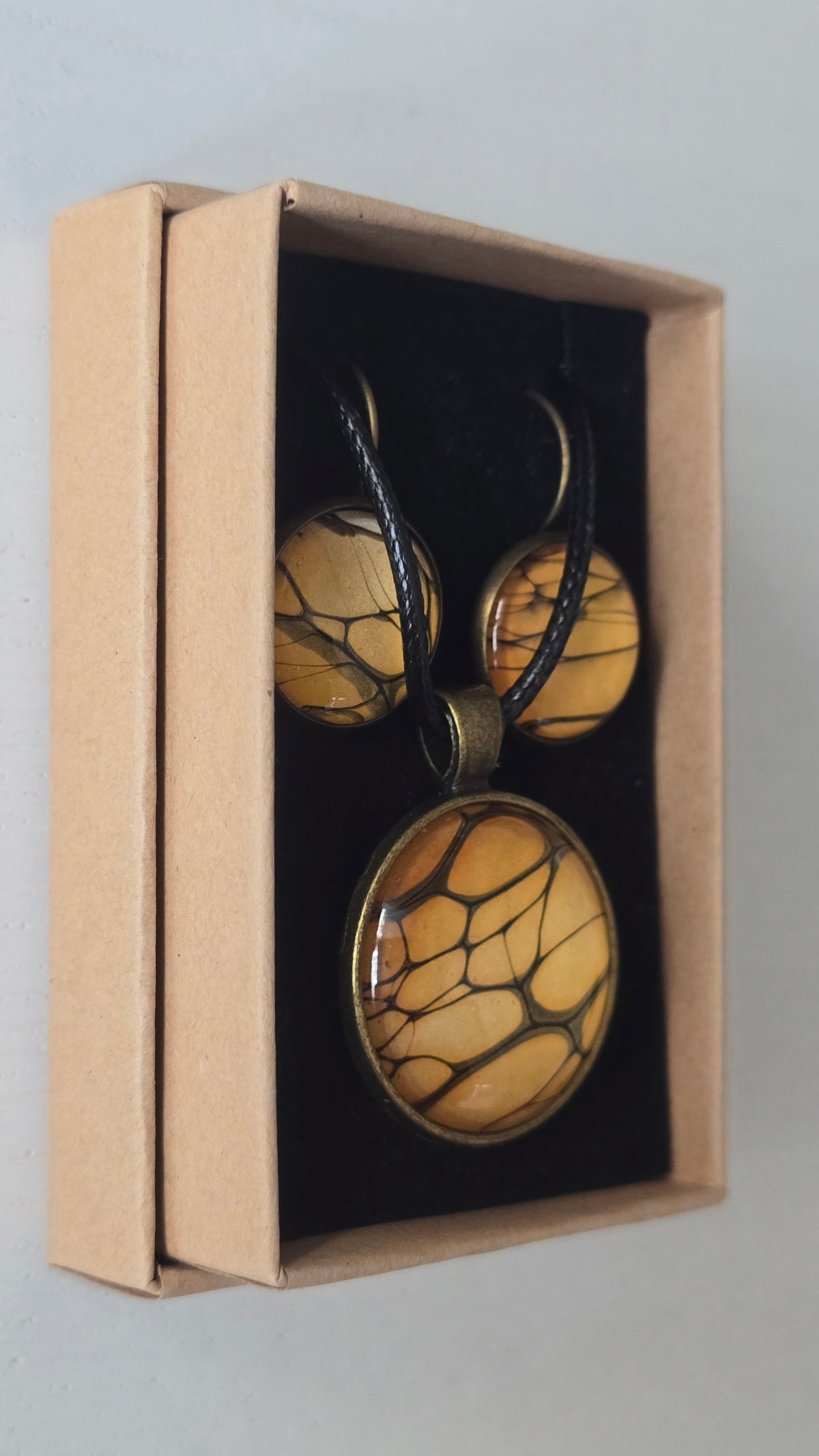 Rundes Cabochon-Schmuckset mit Halskettenanhänger und passenden Ohrringen in warmen Gold- und Bernsteintönen mit feinen dunklen Linien.