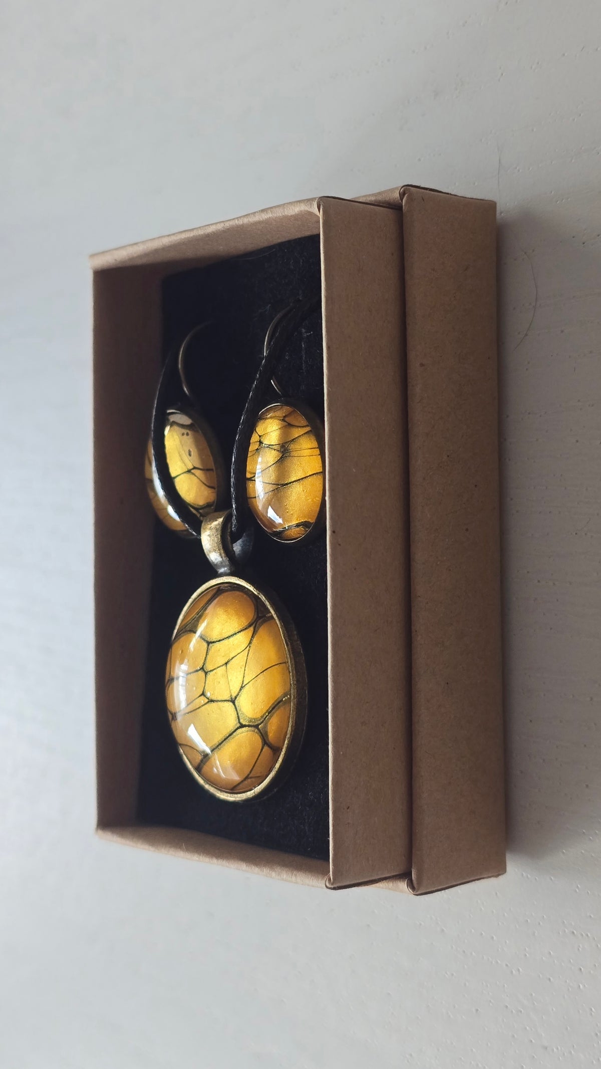 Rundes Cabochon-Schmuckset mit Halskettenanhänger und passenden Ohrringen in warmen Gold- und Bernsteintönen mit feinen dunklen Linien.
