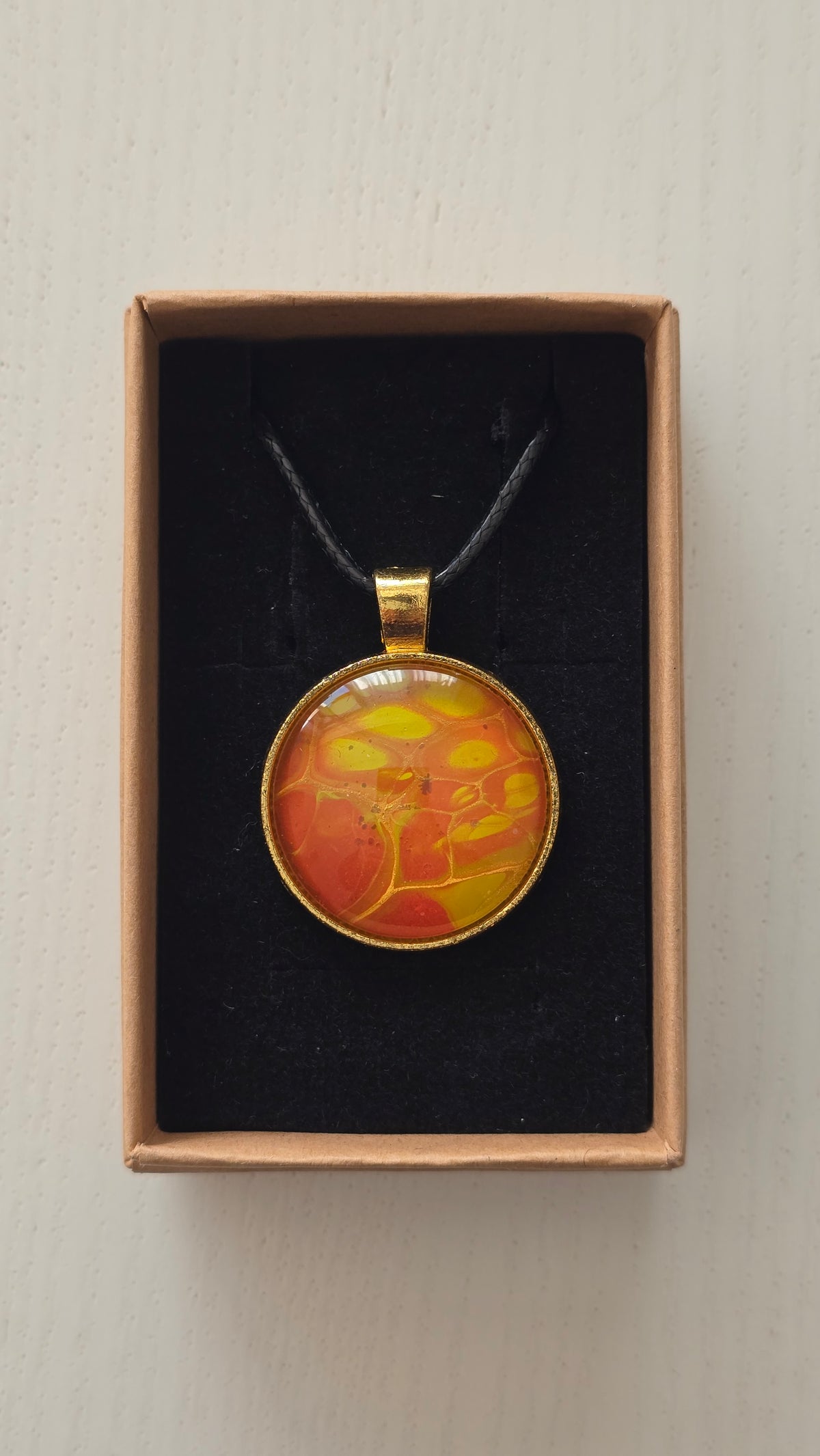 Runde Cabochon Kette Solas Golden Heat mit abstraktem Muster in Orange, Gelb und Gold, goldfarbener Fassung und schwarzem Band.