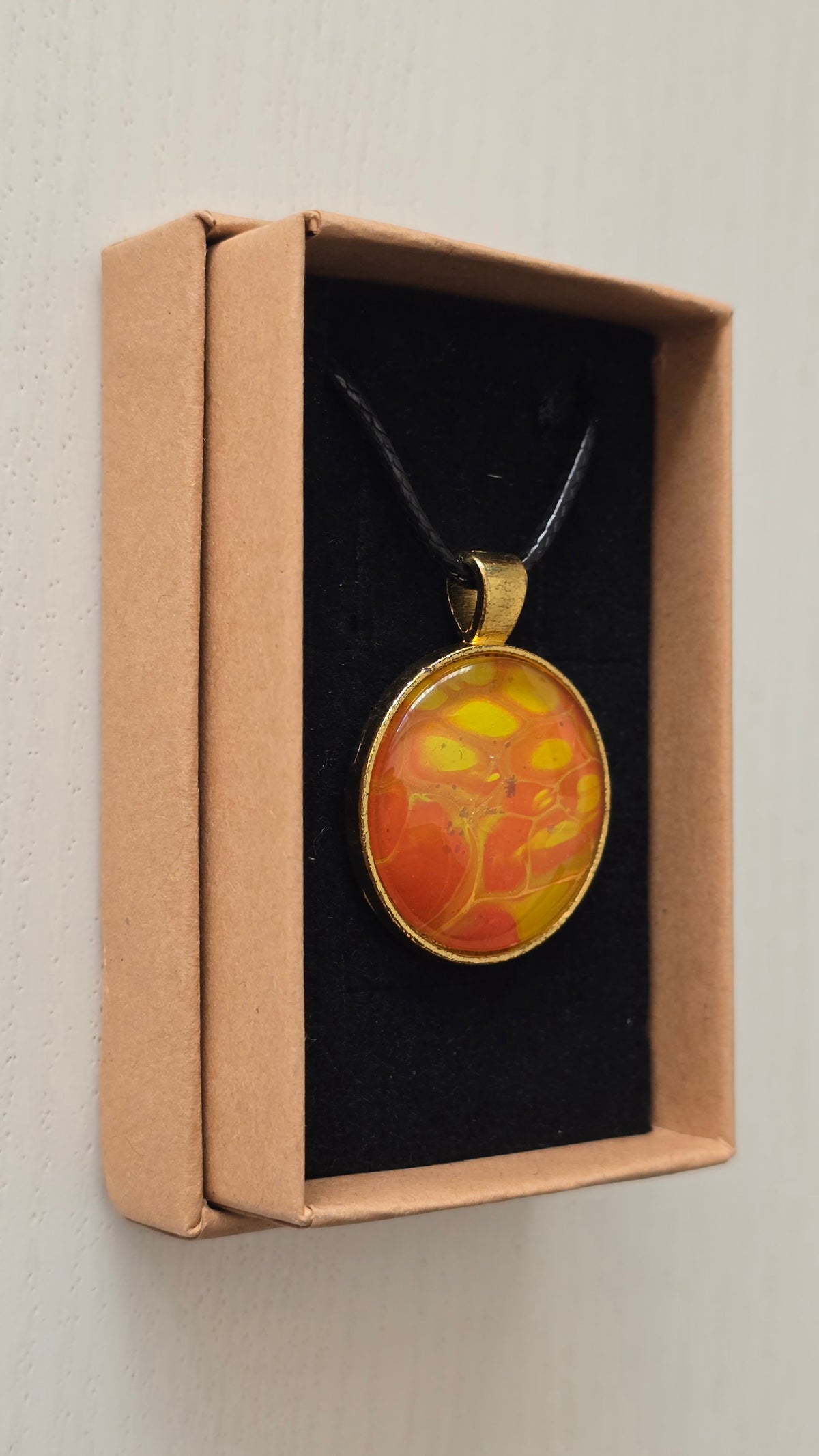 Runde Cabochon Kette Solas Golden Heat mit abstraktem Muster in Orange, Gelb und Gold, goldfarbener Fassung und schwarzem Band.