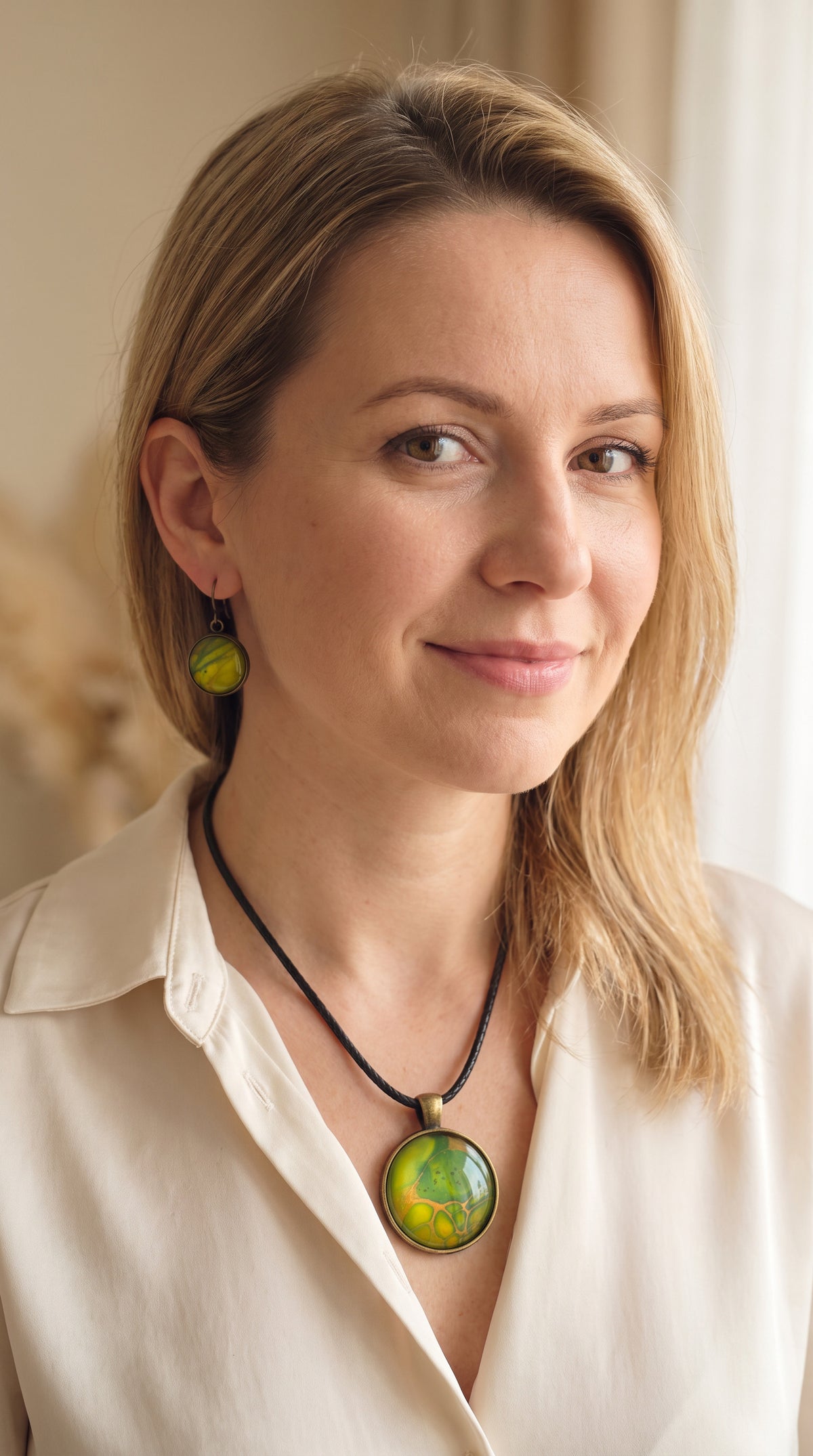 Frau trägt rundes Cabochon Schmuckset mit grossem Kettenanhänger und zwei passenden Ohrringen in Grün, Gelb und Gold mit organisch fliessenden Mustern, bronzefarbenen Fassungen und schwarzem Band.