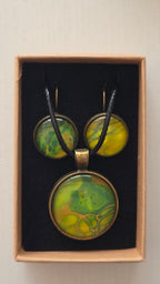 Rundes Cabochon Schmuckset mit grossem Kettenanhänger und zwei passenden Ohrringen in Grün, Gelb und Gold mit organisch fliessenden Mustern, bronzefarbenen Fassungen und schwarzem Band.