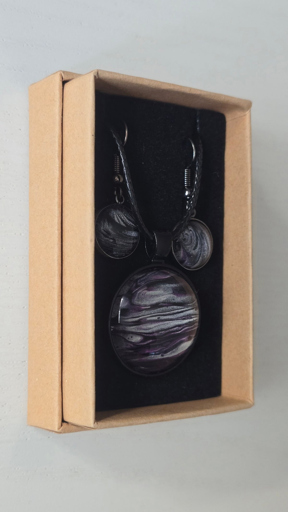 Rundes Cabochon-Schmuckset mit Anhänger und Ohrringen an schwarzem Band, mit geschichtetem Muster in Schwarz, Anthrazit, Violett und silbrigem Schimmer.
