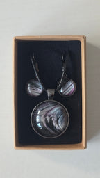 Cabochon-Schmuckset mit rundem Anhänger und zwei Ohrringen in Schwarz und Anthrazit mit geschwungenem silbernem Muster und violetten Akzenten.