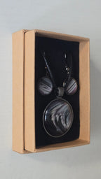 Cabochon-Schmuckset mit rundem Anhänger und zwei Ohrringen in Schwarz und Anthrazit mit geschwungenem silbernem Muster und violetten Akzenten.