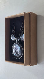 Cabochon-Schmuckset mit rundem Anhänger und zwei Ohrringen in Schwarz und Anthrazit mit geschwungenem silbernem Muster und violetten Akzenten.