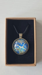 Runder Cabochon-Anhänger an schwarzem Band mit abstraktem, mineralischem Muster in Blau, Türkis, Weiss und Gold.