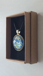 Runder Cabochon-Anhänger an schwarzem Band mit abstraktem, mineralischem Muster in Blau, Türkis, Weiss und Gold.