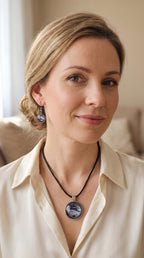 Frau trägt rundes Cabochon-Schmuckset mit Anhänger und Ohrringen an schwarzem Band, mit silbrigem Perlmuttschimmer, Violett und fliessenden schwarzen Linien.