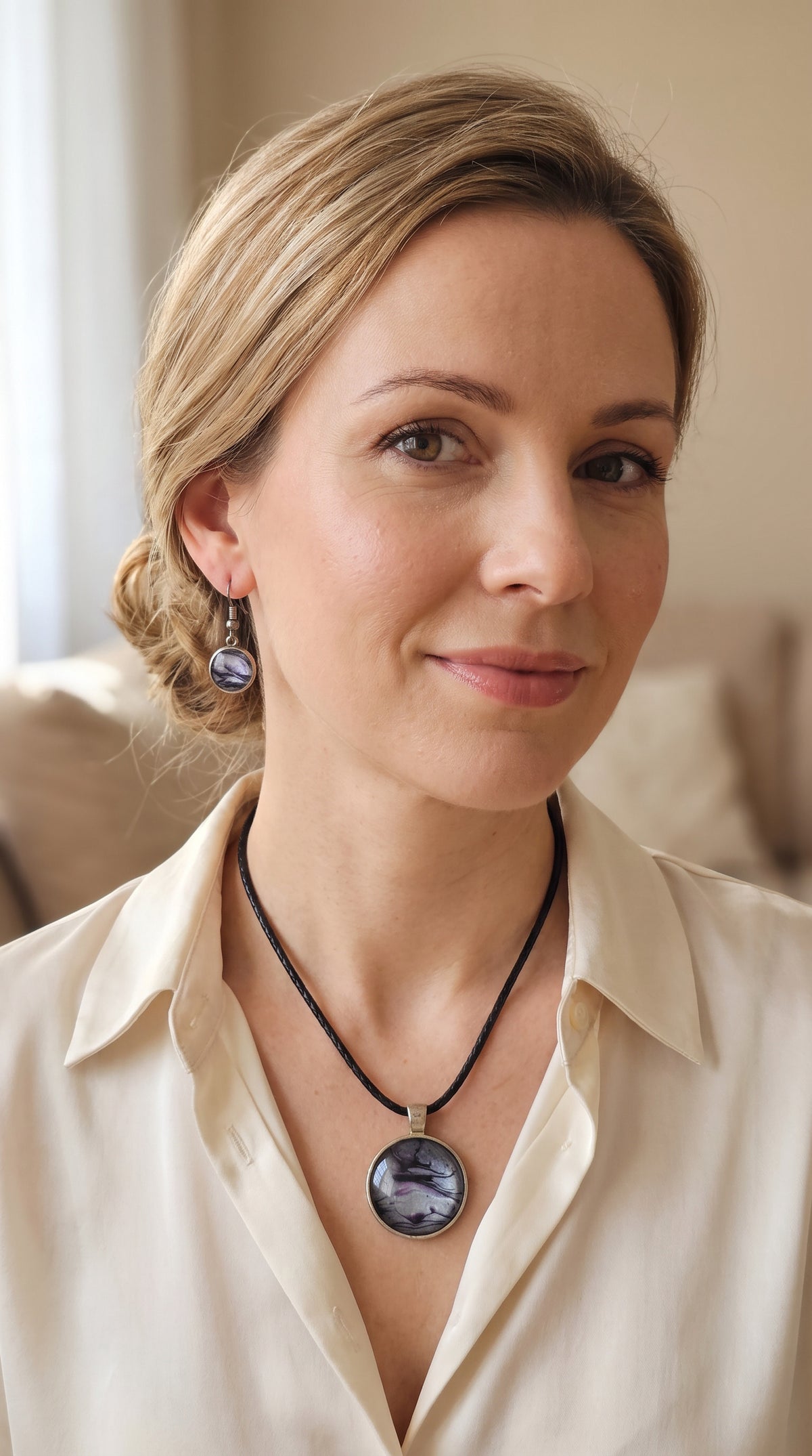Frau trägt rundes Cabochon-Schmuckset mit Anhänger und Ohrringen an schwarzem Band, mit silbrigem Perlmuttschimmer, Violett und fliessenden schwarzen Linien.