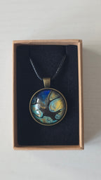 Runder Cabochon-Anhänger an schwarzem Band mit organischem Muster in Türkis, tiefem Blau, Schwarz und warm schimmernden Goldtönen.