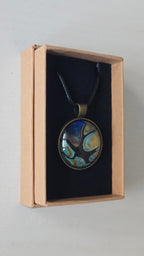 Runder Cabochon-Anhänger an schwarzem Band mit organischem Muster in Türkis, tiefem Blau, Schwarz und warm schimmernden Goldtönen.
