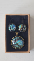 Cabochon-Schmuckset mit rundem Anhänger und zwei Ohrringen mit marmoriertem Muster in Türkis, Petrol, Blau und Schwarz mit goldig-bronzefarbenen Akzenten.