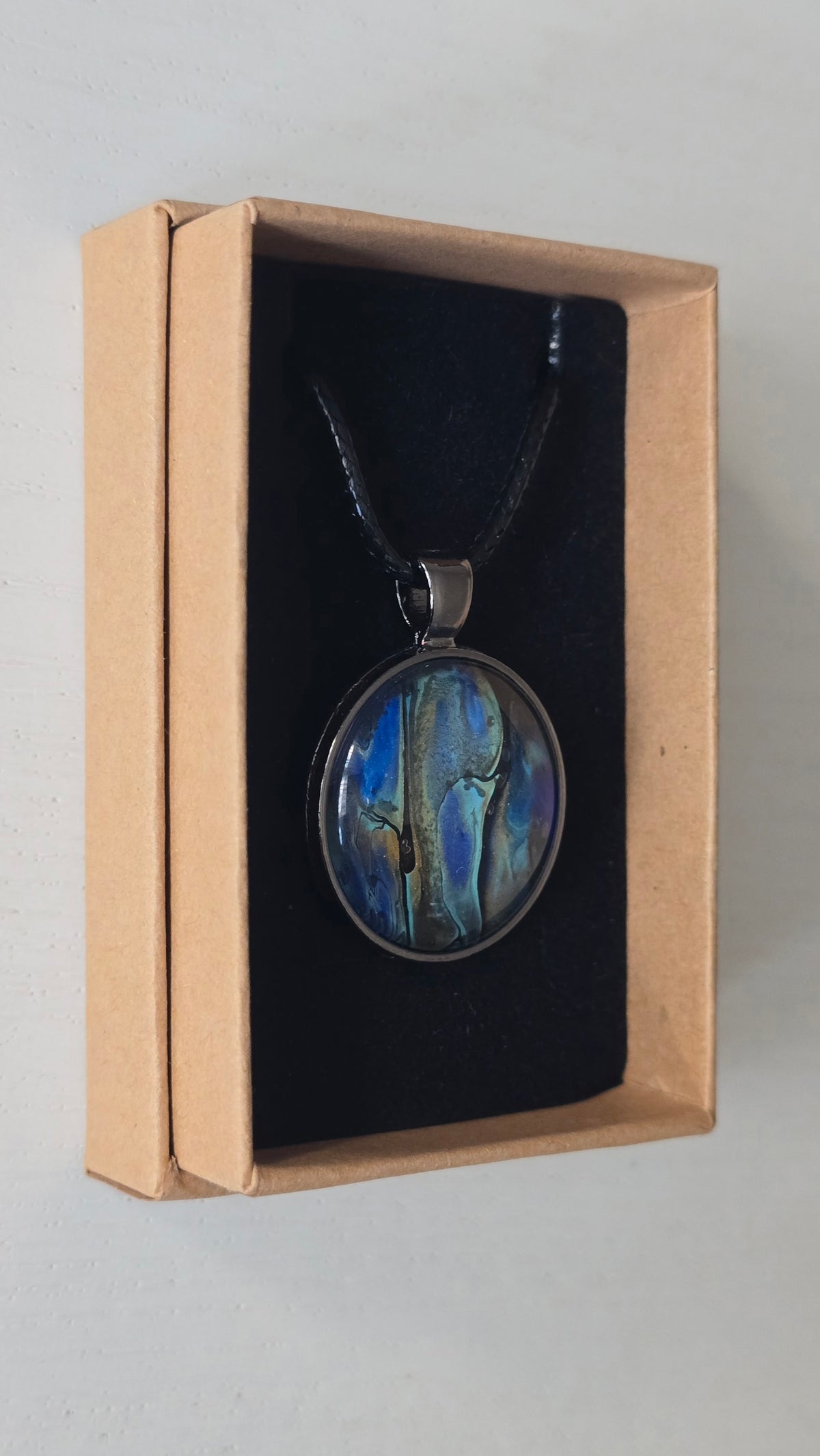 Runde Cabochon Kette Solas Ocean Veil in Blau, Türkis, Petrol und Grün mit dunkler Metallfassung und schwarzem Band.