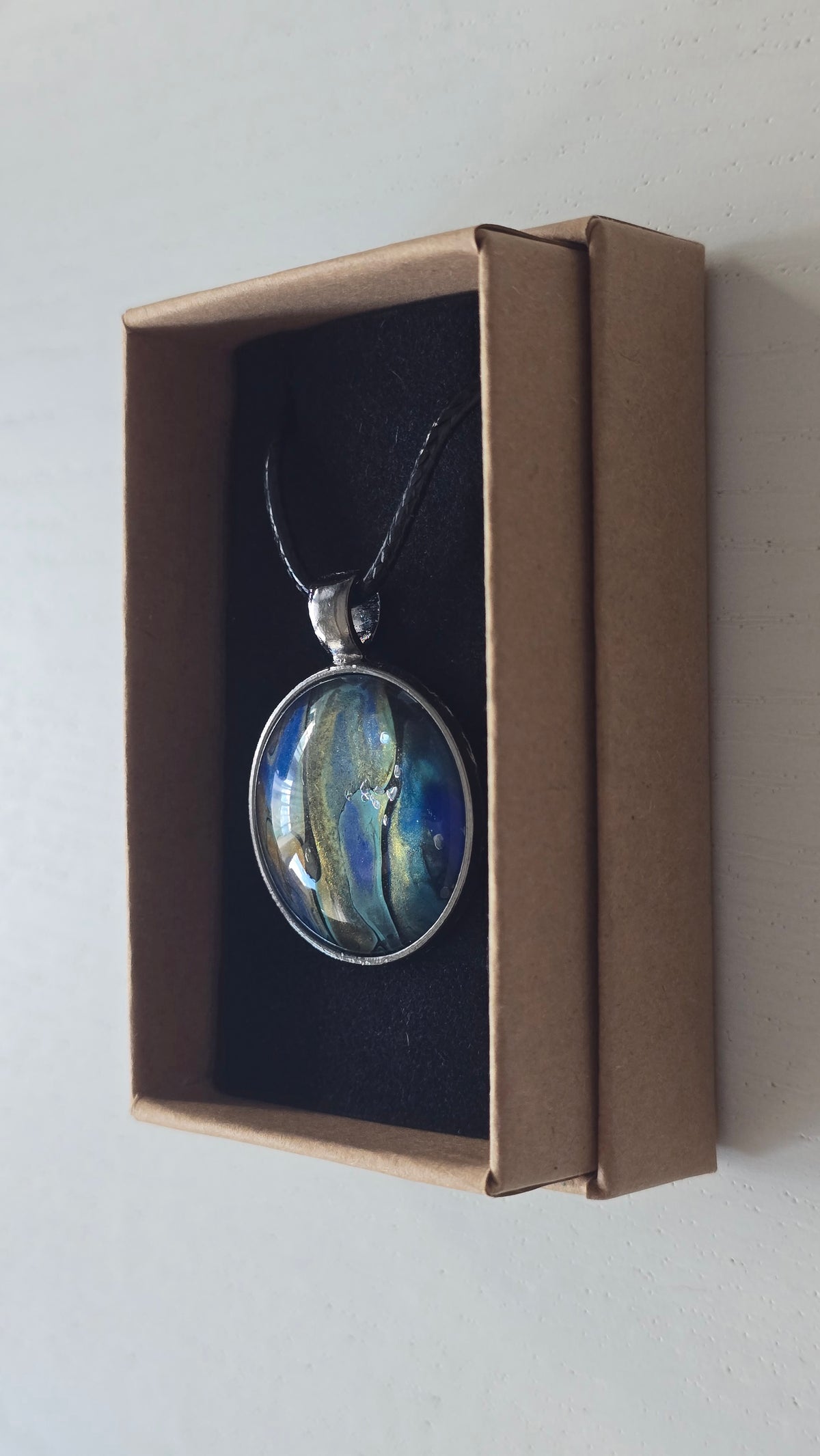 Runde Cabochon Kette Solas Ocean Veil in Blau, Türkis, Petrol und Grün mit dunkler Metallfassung und schwarzem Band.