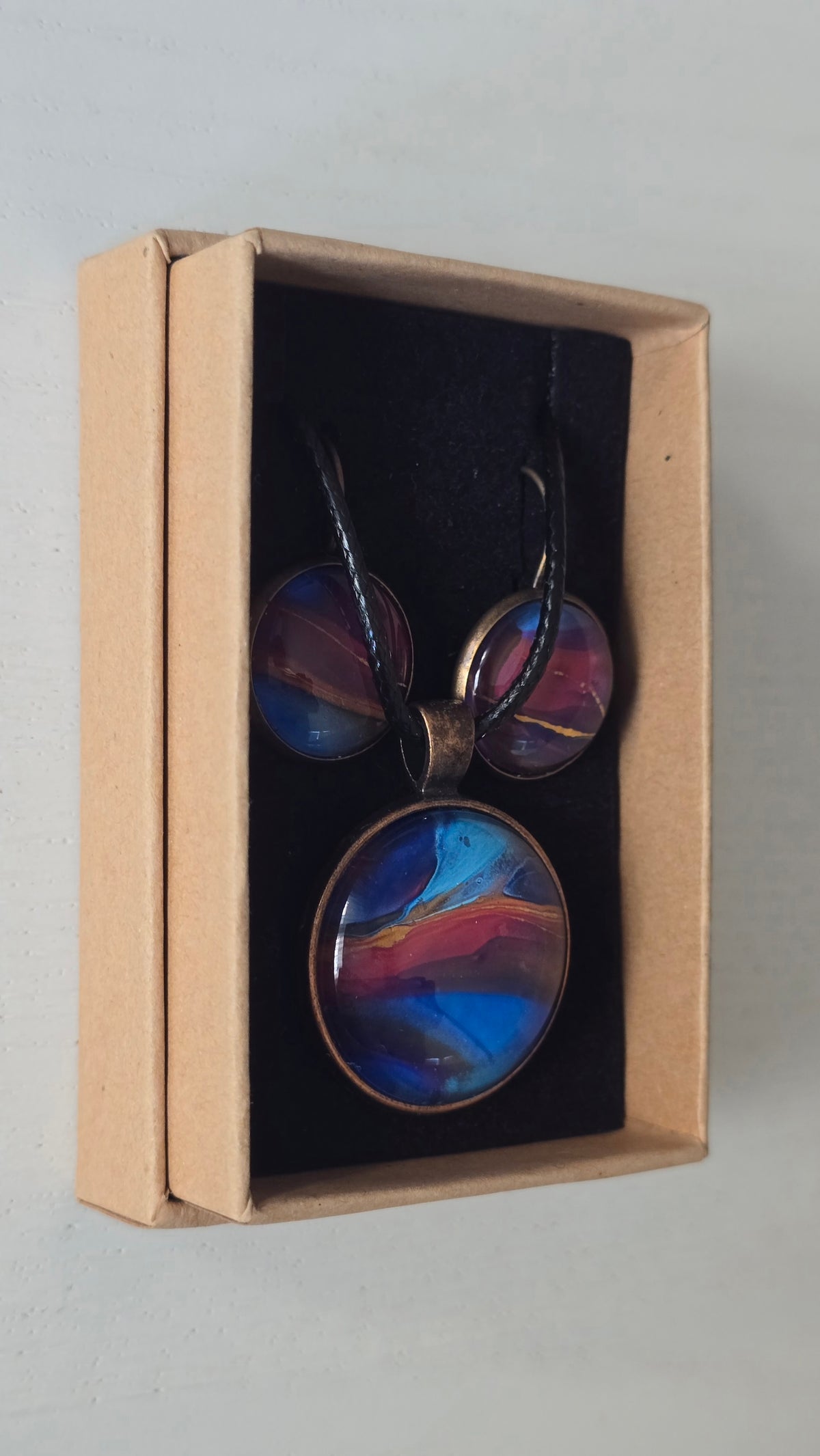 Rundes Cabochon-Schmuckset mit Anhänger und Ohrringen an schwarzem Band, mit abstraktem Muster in Blau, Cyan, Pink und Violett sowie feinen goldenen Linien.