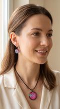 Frau trägt Cabochon-Schmuckset mit rundem Anhänger und zwei Ohrringen in kräftigem Pink und Türkis mit feinen goldenen Zellstrukturen und schwarzem Textilband.