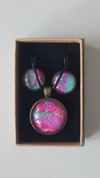 Cabochon-Schmuckset mit rundem Anhänger und zwei Ohrringen in kräftigem Pink und Türkis mit feinen goldenen Zellstrukturen und schwarzem Textilband.