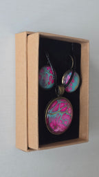 Cabochon-Schmuckset mit rundem Anhänger und zwei Ohrringen in kräftigem Pink und Türkis mit feinen goldenen Zellstrukturen und schwarzem Textilband.