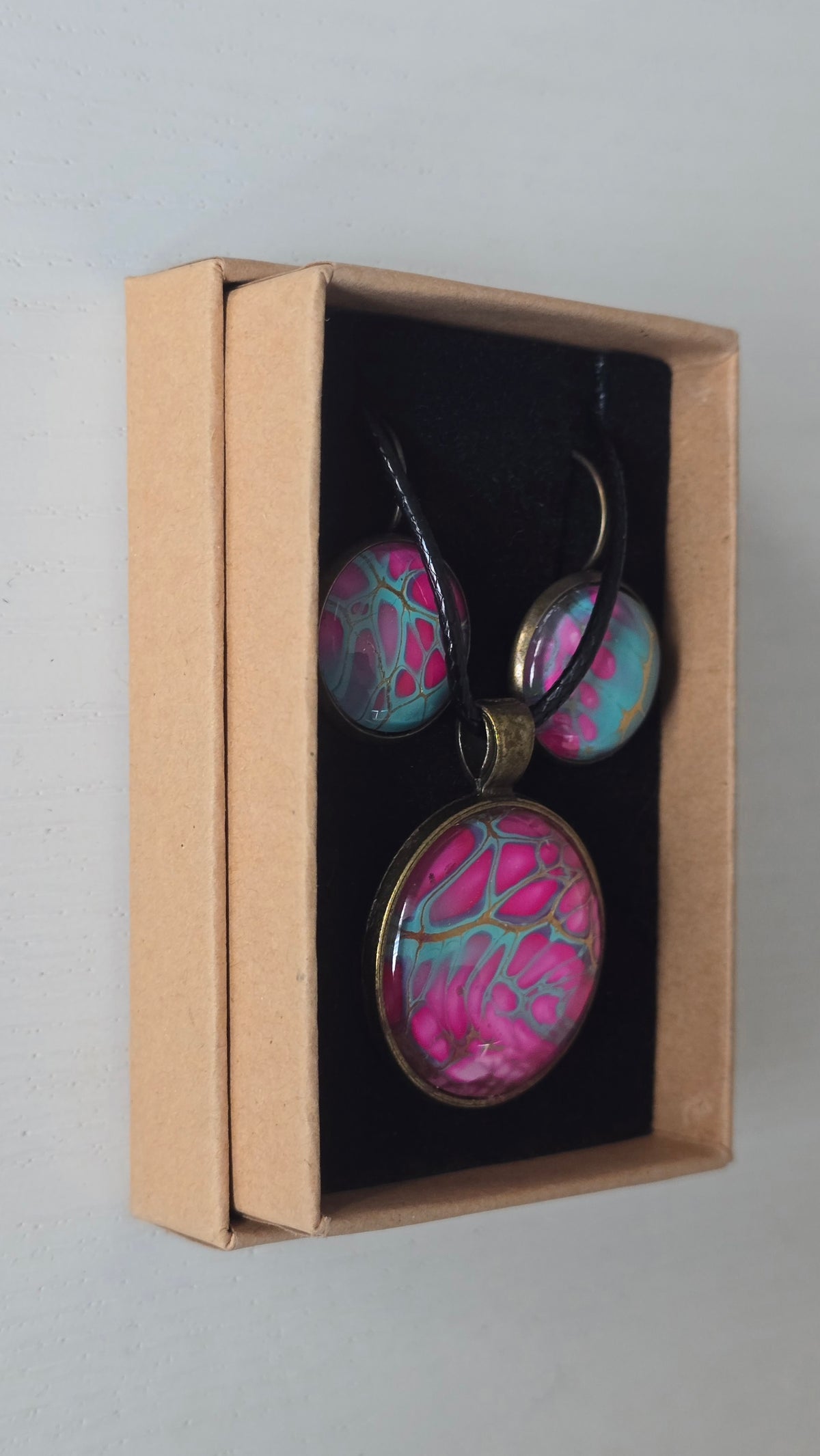 Cabochon-Schmuckset mit rundem Anhänger und zwei Ohrringen in kräftigem Pink und Türkis mit feinen goldenen Zellstrukturen und schwarzem Textilband.