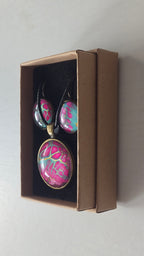 Cabochon-Schmuckset mit rundem Anhänger und zwei Ohrringen in kräftigem Pink und Türkis mit feinen goldenen Zellstrukturen und schwarzem Textilband.